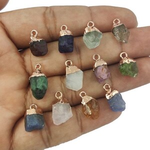 May include: Twelve raw gemstone pendants with rose gold plated caps. The gemstones are various colors, including green, blue, purple, pink, and brown.
