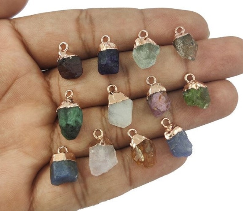May include: Twelve raw gemstone pendants with rose gold plated caps. The gemstones are various colors, including green, blue, purple, pink, and brown.