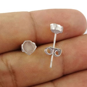 May include: A pair of silver stud earrings with a clear, faceted gemstone. The earrings have a simple, minimalist design.