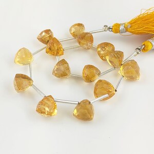 Puede incluir: Una hebra de cuentas de piedras preciosas de color amarillo dorado, cada cuenta tiene forma triangular con un corte facetado. Las cuentas están enhebradas en un alambre de plata y tienen un borla al final.