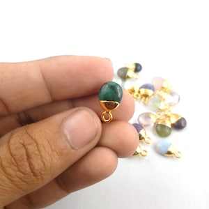 May include: A green gemstone pendant with a gold bail. The pendant is oval shaped and has a smooth, polished surface. The pendant is held in a hand against a white background.