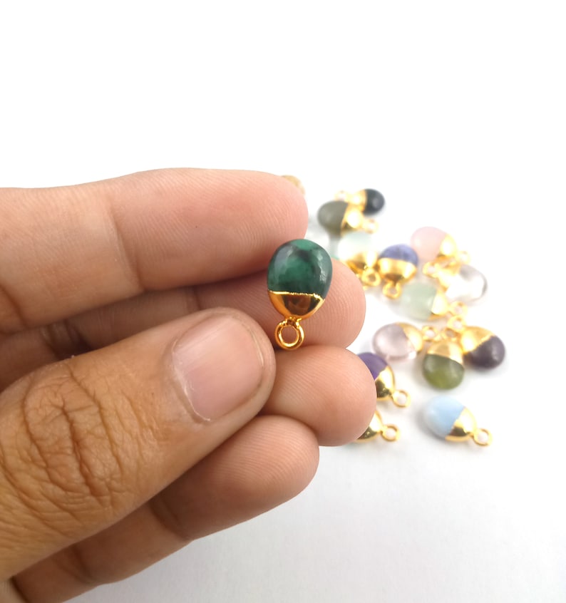 May include: A green gemstone pendant with a gold bail. The pendant is oval shaped and has a smooth, polished surface. The pendant is held in a hand against a white background.