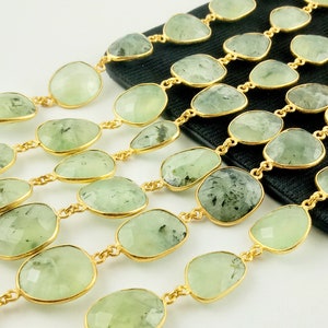 May include: A strand of green gemstone beads with gold accents. The beads are oval shaped and have a light green color with dark green inclusions. The beads are strung on a gold chain.
