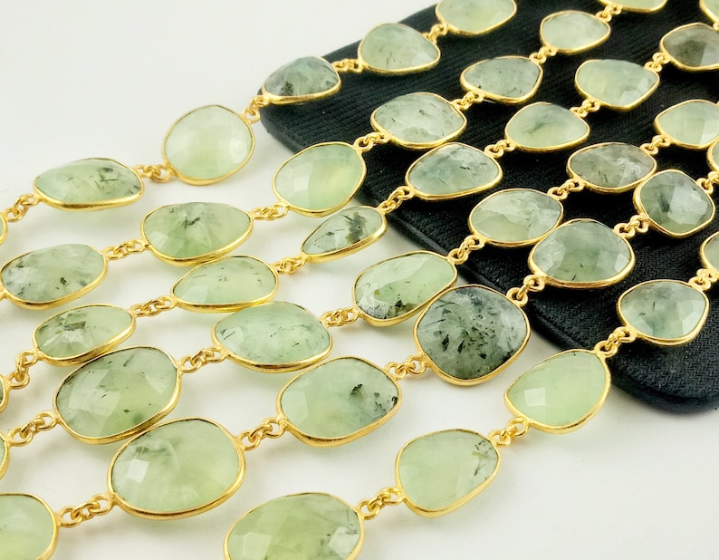 May include: A strand of green gemstone beads with gold accents. The beads are oval shaped and have a light green color with dark green inclusions. The beads are strung on a gold chain.