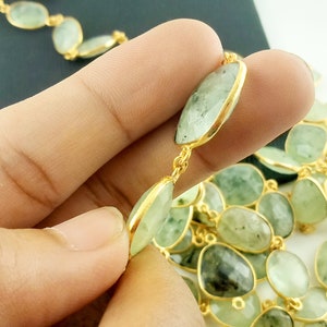 May include: A gold chain necklace with green gemstone beads. The beads are oval shaped and have a slightly irregular shape. The chain is made of small, round links.