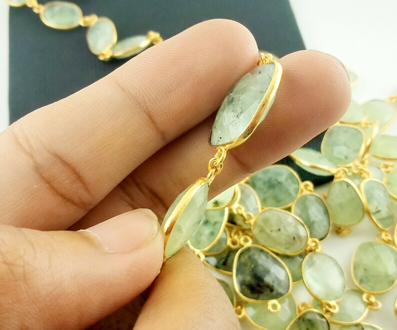 May include: A gold chain necklace with green gemstone beads. The beads are oval shaped and have a slightly irregular shape. The chain is made of small, round links.