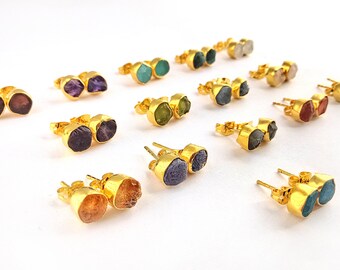 Puede incluir: Un conjunto de pendientes de botón dorados con diferentes piedras naturales. Los pendientes presentan una variedad de colores, incluyendo morado, verde, azul y naranja. Las piedras están engastadas en biseles dorados.