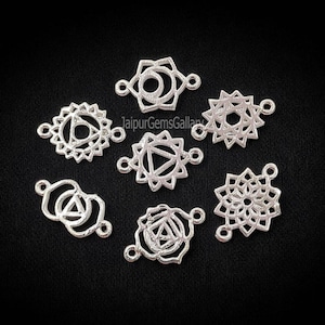 Puede incluir: Encantos de chakra plateados con intrincados diseños geométricos. Cada amuleto presenta un patrón único, que incluye círculos, triángulos y elementos florales, con pequeños bucles para la fijación. Los amuletos se muestran sobre un fondo negro.