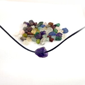 May include: A purple amethyst crystal pendant on a black cord necklace. The pendant is a rough, natural shape.