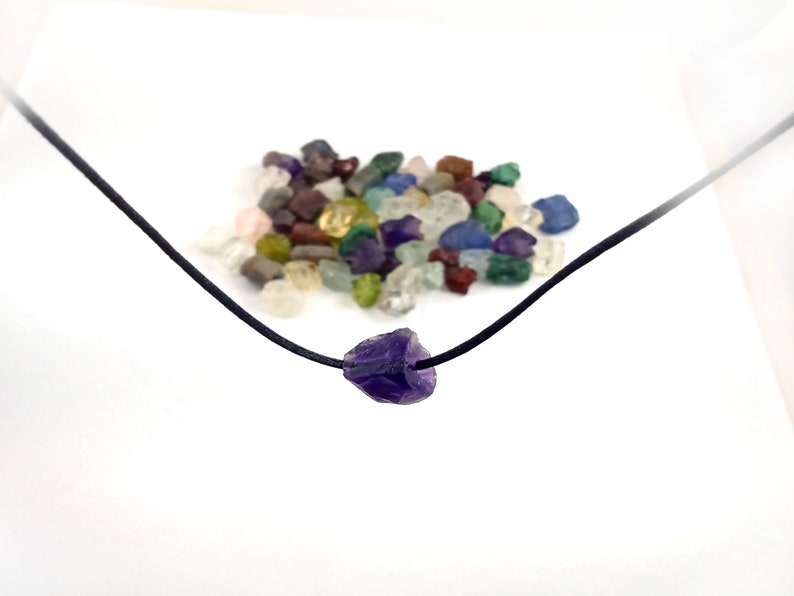 May include: A purple amethyst crystal pendant on a black cord necklace. The pendant is a rough, natural shape.