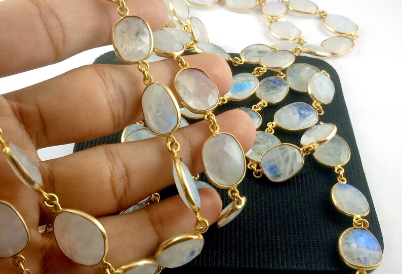 Peut inclure: Un collier en cha&icirc;ne dor&eacute;e avec des perles de pierre de lune de forme ovale. Les perles sont de couleur blanc laiteux avec un l&eacute;ger reflet iridescent.