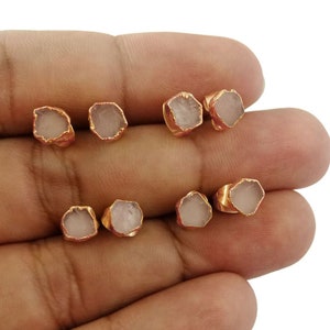 May include: Six pairs of rose quartz earrings with gold-toned settings. The earrings are displayed on a hand.