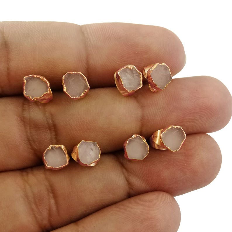 May include: Six pairs of rose quartz earrings with gold-toned settings. The earrings are displayed on a hand.