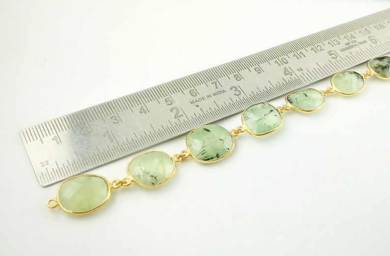 May include: A gold chain bracelet with green gemstone beads. The bracelet is measured against a ruler, showing the beads are approximately 1 inch in size.