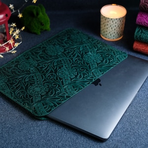 K&ouml;nnte beinhalten: Eine gr&uuml;ne Lederh&uuml;lle f&uuml;r Laptops mit einem komplizierten Blumenmuster. Die H&uuml;lle ist geschlossen und ein silberner Laptop ist teilweise im Inneren sichtbar.