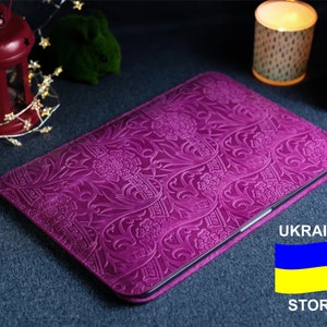 K&ouml;nnte beinhalten: Eine violette Lederh&uuml;lle f&uuml;r Laptops mit einem gepr&auml;gten Blumenmuster. Die H&uuml;lle ist geschlossen und die Kanten sind sichtbar. Der Hintergrund ist eine dunkelblaue Oberfl&auml;che. Der Text "UKRAINE STORE" und die ukrainische Flagge sind in der unteren rechten Ecke des Bildes sichtbar.
