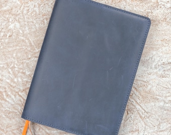 May include: A rectangular notebook cover made of smooth, matte navy blue leather. The cover features visible stitching along the edges and a bright orange ribbon bookmark extending from the bottom left corner of the closed item.