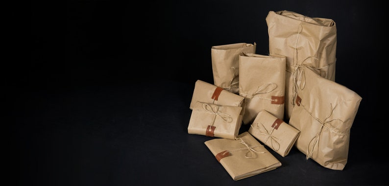 K&ouml;nnte beinhalten: Eine Gruppe brauner Papierpakete, die mit Schnur gebunden und mit braunen Lederetiketten versiegelt sind. Die Pakete sind auf einer schwarzen Oberfl&auml;che angeordnet.