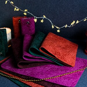 K&ouml;nnte beinhalten: Ein Set aus sechs Leder-Schl&uuml;sselanh&auml;ngern in verschiedenen Farben, darunter Burgunder, Gr&uuml;n und Braun. Jeder Schl&uuml;sselanh&auml;nger hat ein einzigartiges, gepr&auml;gtes Blumenmuster und einen Metall-Druckknopfverschluss.