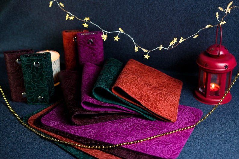 K&ouml;nnte beinhalten: Ein Set aus sechs Leder-Schl&uuml;sselanh&auml;ngern in verschiedenen Farben, darunter Burgunder, Gr&uuml;n und Braun. Jeder Schl&uuml;sselanh&auml;nger hat ein einzigartiges, gepr&auml;gtes Blumenmuster und einen Metall-Druckknopfverschluss.