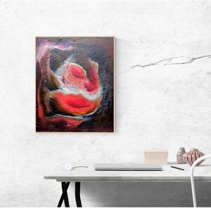 May include: Abstract painting of a red and white flower with a dark background. The painting is framed in a gold frame and is hanging on a white wall.