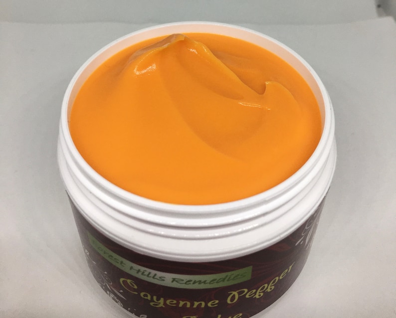 May include: A close-up of a jar of orange-colored cream with the text "West Hills Remedies Cayenne Pepper" on the label.