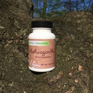 May include: A white bottle with a black lid and a brown label that says "Forest Hills Remedies Ashwagandha Herbal Supplement 60 Veg. Capsules"