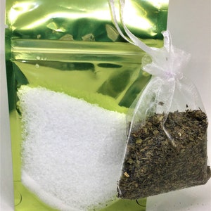 May include: A green resealable pouch with a white zipper contains white bath salts. A white mesh bag with a lavender ribbon contains dried herbs.