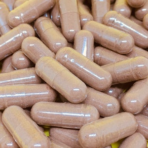 May include: A close-up image of a pile of brown capsules. The capsules are translucent and filled with a brown powder.