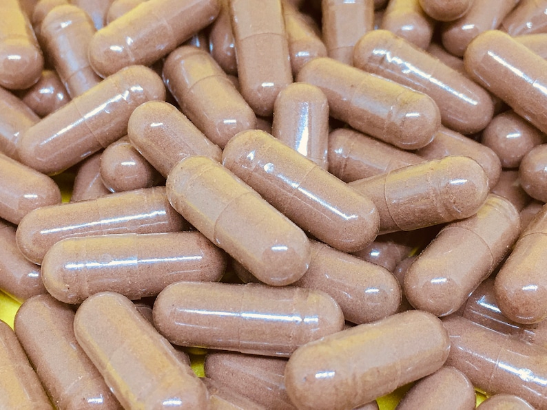 May include: A close-up image of a pile of brown capsules. The capsules are translucent and filled with a brown powder.