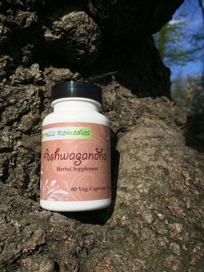 May include: A white bottle with a black lid labeled "Ashwagandha Herbal Supplement 60 Veg. Capsules" by "The Hills Remedies". The bottle is sitting on a tree trunk.