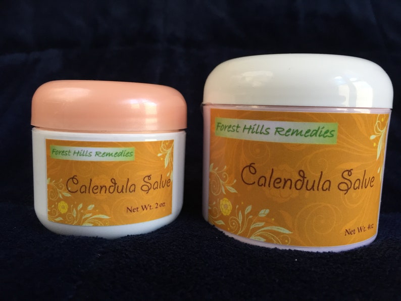May include: Two white jars with orange labels. The labels read "Forest Hills Remedies Calendula Salve". The smaller jar is labelled "Net Wt. 2 oz" and the larger jar is labelled "Net Wt. 4 oz".