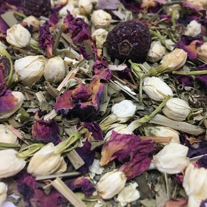 Op de afbeelding: Een close-up van een mengsel van gedroogde kruiden en bloemen voor thee. De mix bevat gedroogde rozenblaadjes, jasmijnknoppen en groene bladeren.