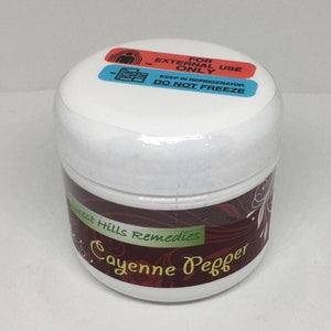 May include: A white jar with a red and green label that reads "Forest Hills Remedies Cayenne Pepper". The jar has a blue and red sticker on the lid that reads "For External Use Only Keep in Refrigerator Do Not Freeze".