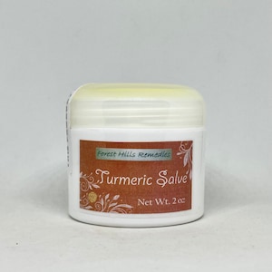 Puede incluir: Un tarro blanco con tapa amarillo claro, etiquetado "Forest Hills Remedies Turmeric Salve". La etiqueta marrón tiene texto blanco y adornos florales. Peso neto: 57 gramos.