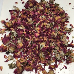 May include: A pile of dried rose petals in shades of pink, red, and brown. The petals are scattered on a white surface.