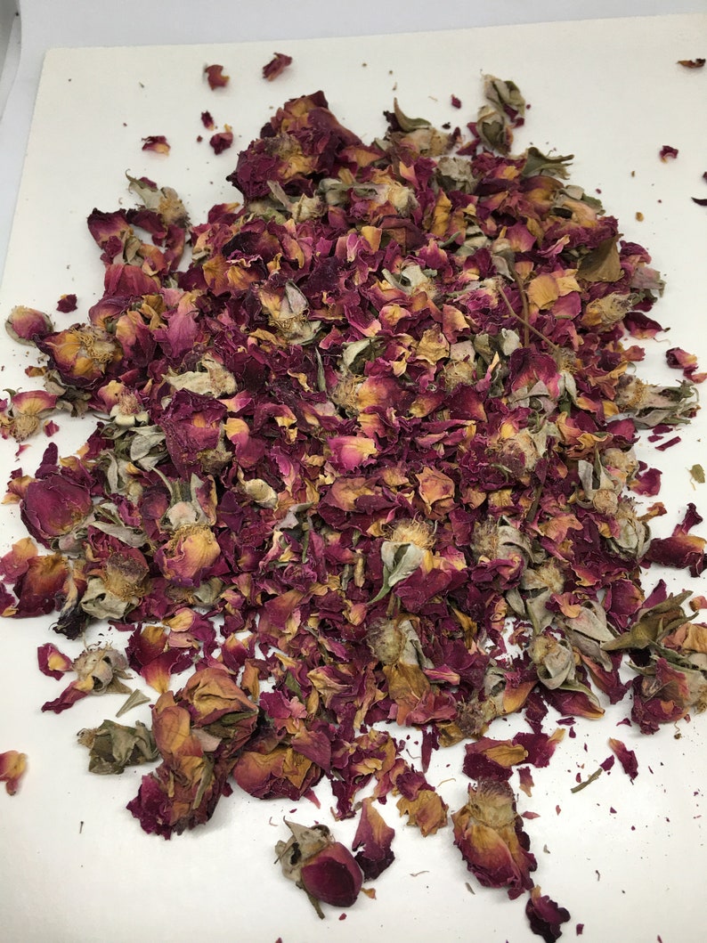 May include: A pile of dried rose petals in shades of pink, red, and brown. The petals are scattered on a white surface.