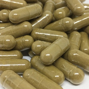 May include: A close-up of a pile of brown capsules. The capsules are made of clear plastic and contain a brown powder.