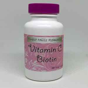 May include: A white bottle with a purple cap labeled "Vitamin C Biotin" from Forest Hills Remedies. The label is pink with white floral accents. The bottle contains 90 vegetarian capsules.