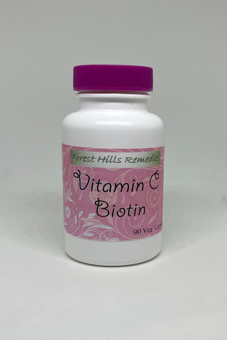 May include: A white bottle with a purple cap labeled "Vitamin C Biotin" from Forest Hills Remedies. The label is pink with white floral accents. The bottle contains 90 vegetarian capsules.