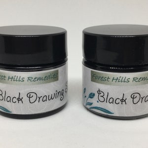 May include: Two small black jars with white labels that read "Forest Hills Remedies Black Drawing Salve".