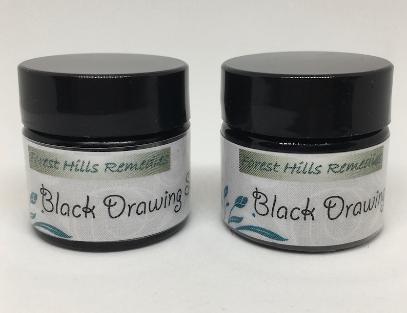 May include: Two small black jars with white labels that read "Forest Hills Remedies Black Drawing Salve".