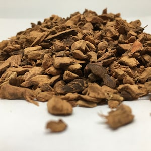 May include: A pile of dried, brown, and slightly reddish-brown bark chips. The chips are irregularly shaped and have a rough texture.