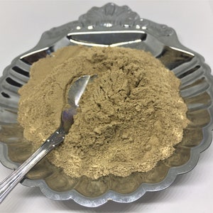 May include: A close-up of a pile of light brown powder in a silver shell-shaped dish with a silver spoon.