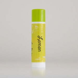 Puede incluir: Un tubo de bálsamo labial amarillo con una tapa verde y la palabra "Lemon" escrita en cursiva negra en la etiqueta.