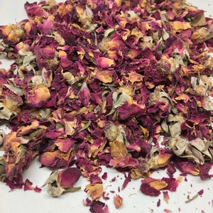 May include: A pile of dried rose petals and buds in shades of pink, red, and beige. The petals are scattered on a white surface.