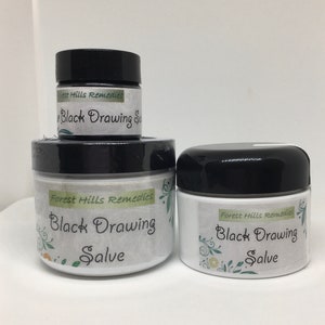 May include: Three jars of black drawing salve, labeled "Forest Hills Remedies Black Drawing Salve". The jars are white with black lids and feature a green floral design.