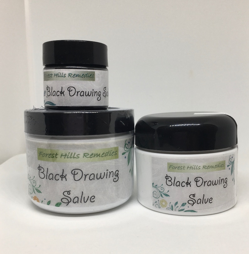 May include: Three jars of black drawing salve, labeled "Forest Hills Remedies Black Drawing Salve". The jars are white with black lids and feature a green floral design.