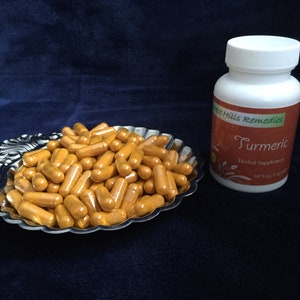 Op de afbeelding: Een zilveren dienblad gevuld met oranje kurkuma capsules. Naast het dienblad staat een witte fles met een bruin etiket waarop "Forest Hills Remedies Kurkuma Herbal Supplement 60 Veg Caps" staat.