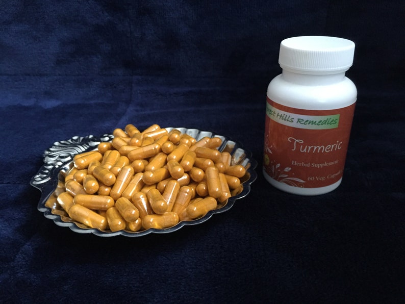 Op de afbeelding: Een zilveren dienblad gevuld met oranje kurkuma capsules. Naast het dienblad staat een witte fles met een bruin etiket waarop "Forest Hills Remedies Kurkuma Herbal Supplement 60 Veg Caps" staat.
